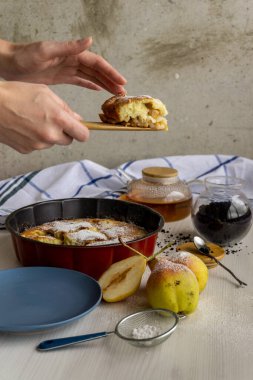 Önünde armutlar olan beyaz bir masada mavi bir tabakta çay için bir parça armutlu turta. Dikey.