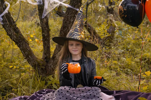 Funny niña en un disfraz de bruja para Halloween sostiene una taza en forma de calabaza. —  Fotos de Stock