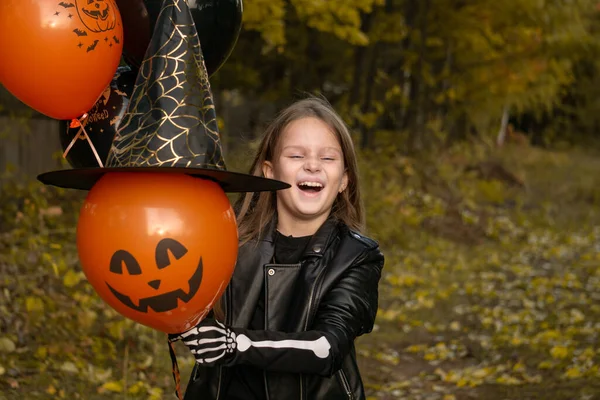 Divertido niña en un disfraz de bruja para Halloween poner un sombrero en un globo naranja y se ríe. —  Fotos de Stock