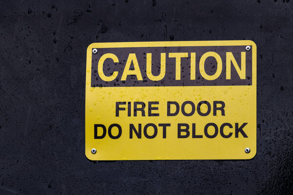 Вид желтого знака Осторожно Пожарная дверь Не блокировать на черном фоне