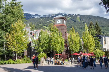 Whistler, Kanada - 5 Temmuz 2020: Güneşli bir günde arka planda dağ manzaralı Whistler Village dolusu insan. Seçici odak