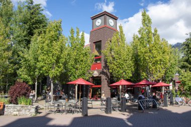 Whistler, Kanada - 5 Temmuz 2020: Güneşli bir günde arka planda dağ manzaralı Whistler Village dolusu insan. Seçici odak