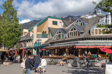 Whistler, Kanada - 5 Temmuz 2020: Güneşli bir günde arka planda dağ manzaralı Whistler Village dolusu insan