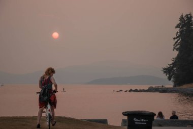 Vancouver, Kanada - 1.2021 Ağustos: Vancouver üzerinde Smokey Sky. Fotoğraf, Stanley Park 'ın ikinci plajında gün batımında etrafı sis ve dumanla çevrili kadını gösteriyor.