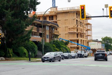 Vancouver, Kanada - 25 Eylül 2025: Kuzey Vancouver 'da kentsel yapı: kontrplak çerçeveli çok katlı apartman dairesi, yeşilliklerin ortasında yükseliyor, mavi vinç kaldırma malzemeleri