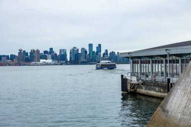 Vancouver, Kanada - 25 Eylül 2025: Vancouver gökdelenleri ve Kanada Yerleşkesi, mavi Seabus feribotu bulutlu günde sakin limanı geçiyor