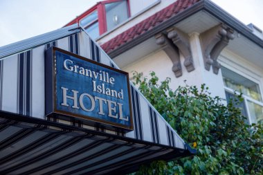 Vancouver, Kanada - 6 Ekim 2025: Granville Island Oteli mavi mahsul tabelası beyaz süslemeli, dekoratif mimari detaylı ve yeşil yapraklı bir binanın üzerine asıldı