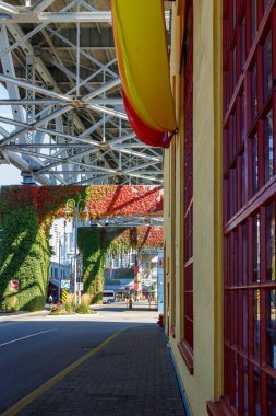 Vancouver, Kanada - 6 Ekim 2025: Renkli sarı su kaydırağıyla Granville Adası sokak manzarası, kırmızı çerçeveli bina, köprü yapısı, yeşil duvarlar ve kentsel Vancouver arkaplanı