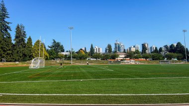 Vancouver, Kanada - 26 Ağustos 2025: Mahon Park North Vancouver 'da hedefleri, projektörleri, oyuncuları ve şehir silueti olan yeşil yapay saha