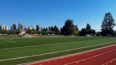 Vancouver, Kanada - 26 Ağustos 2025: Mahon Park North Vancouver 'da hedefleri, projektörleri, oyuncuları ve şehir silueti olan yeşil yapay saha