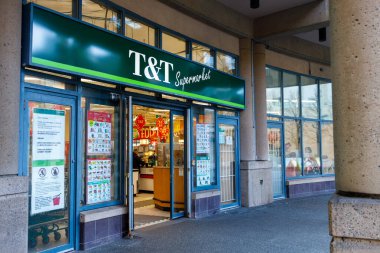 Vancouver, Kanada - 2 Mart 2026: Yeşil tabelalı ve Çince harfli T & T süpermarket vitrinleri, sokak lambasında kırmızı panda pankartları