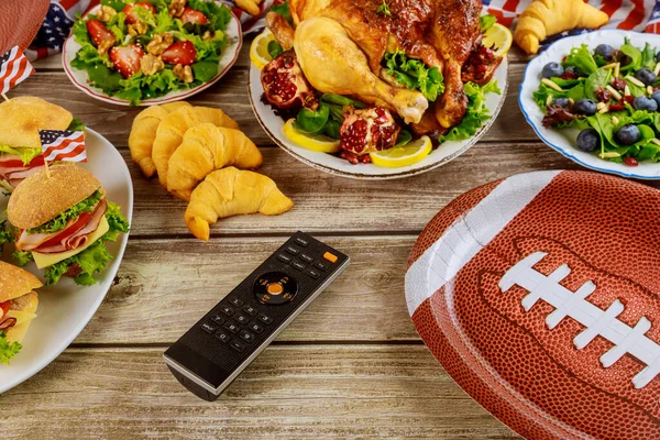 Party table with remote control for sport watching american football game on tv.