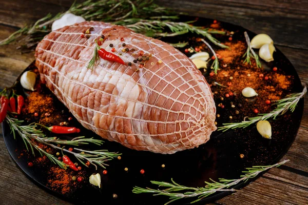 Raw fresh pork shoulder with spices on black wooden board. Holiday food. Close up.