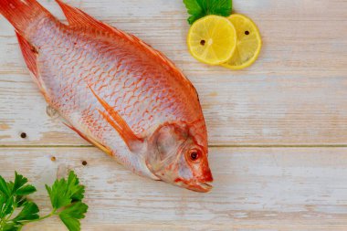 Çiğ kırmızı tilapia balığı, otlu, limonlu ve ahşap arka planda. Üst görünüm, alanı kopyala.