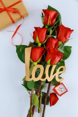 Bir buket güzel kırmızı gülün üzerinde aşk kelimesi. Yüzük ve hediyeyle. Sevgililer Günü mü Anneler Günü mü?.