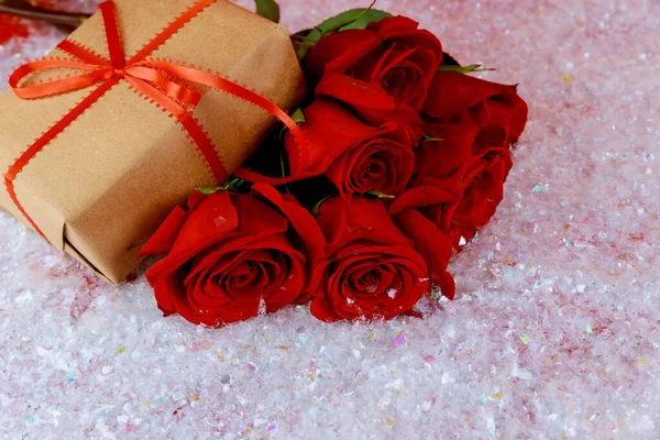 Present and bouquet of beautiful red roses on sparkle snow. Mothers Day or Valentines Day concept..