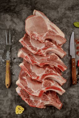 Koyu arkaplanda çatal ve bıçak ile taze domuz pirzolası. Üst görünüm.