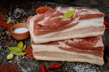 Koyu arkaplanlı baharatlı çiğ domuz göbeği. Kapat..