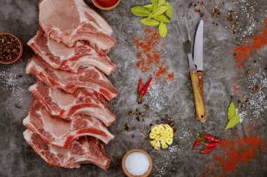 Çiğ domuz pirzolası, baharat ve gri arka planda bıçak dilimliyor. Üst görünüm.