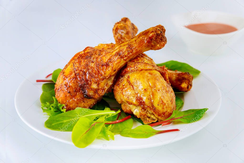 Spicy chicken drumsticks with spinach on white plate.
