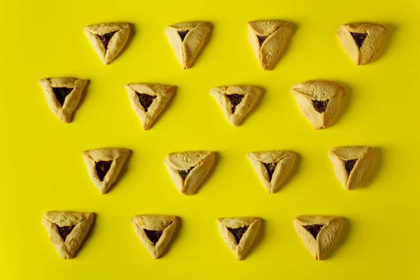 Baked hamantaschen jewish cookies with jam on yellow surface for Purim.