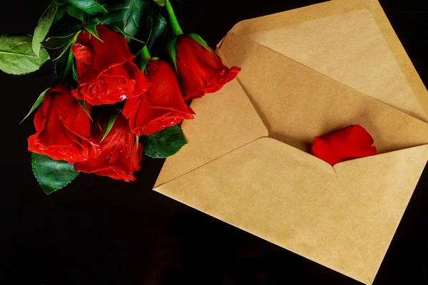 Envelope and bouquet of red roses on black table. Valentines day concept.