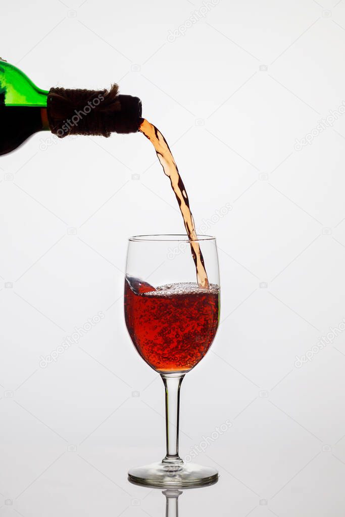 Pouring red wine into clear glass on white background.