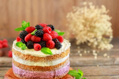 Ahşap arka planda taze ahududu ve böğürtlenlerle süslenmiş çok güzel bir pasta..