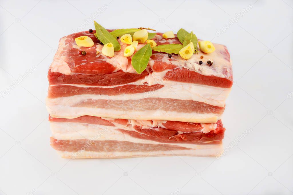 Two pieces of raw pork belly with garlic and bay leaves isolated on white background.