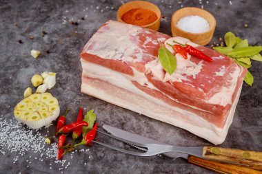 Sarımsaklı kemiksiz çiğ domuz göbeği ve koyu arkaplanda defne yaprakları..