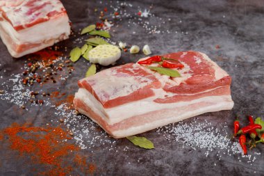 Sarımsaklı kemiksiz çiğ domuz göbeği ve koyu arkaplanda defne yaprakları..