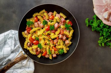 Renkli makarna rotini, kirazlı domates ve tavada jambon. Üst görünüm.