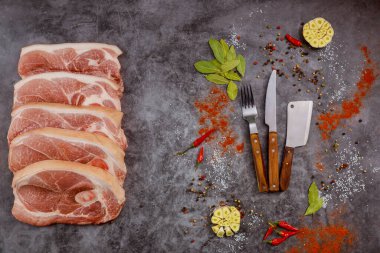 Çiğ domuz pirzolası, baharatlı et ve gri arka planda bıçak dilimliyor. Üst görünüm.
