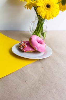 Pembe çörekler, sarı çiçekler, sarı ve bej arka planda.