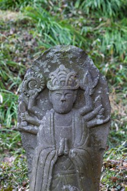 Üzerinde Murti figürü olan küçük yıpranmış Buda heykeli plaketi, Japonya 'daki Aso Kumamoto kasabasındaki Saigandenji Tapınağı' nda farklı güçleri sembolize eden birkaç yüz ve kol.
