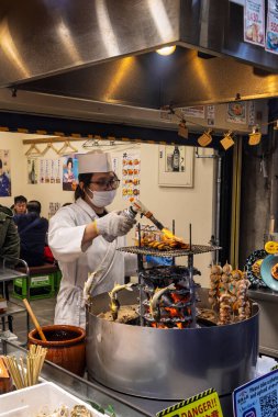 Osaka, Japonya - 30 Mart 2025: Yüzü maskeli kadın taze deniz ürünleri hazırlıyor, Kuromon Ichiba Balık Pazarı, Osaka, Japonya