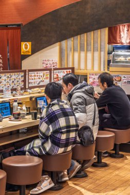 Osaka, Japonya - 31 Mart 2025: Kaiten Beltin Osaka ile suşi restoranında peş peşe üç adam