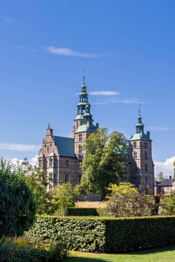 Rosenborg Kalesi 'nin tuğladan duvarları ve budanmış çitlerin ve ağaçların üzerinden yükselen bakır yeşil kulelerin manzarası. Danimarka 'nın Kopenhag kentindeki Rönesans mimarisinin sergilendiği barışçıl Avrupa tarihi simgesi.