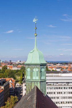 A dramatic view of a green copper spire atop a historic church in Copenhagen, Denmark, with a panoramic cityscape and blue sky. Ideal for architecture, travel, and European city imagery.