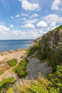 Danimarka 'daki Hovs Hallar Doğa Rezervi' nde dramatik bir kıyı manzarası: engebeli uçurumlar, kayalık plaj ve mavi gökyüzü altında beyaz bulutlar, tepe boyunca yeşillik.