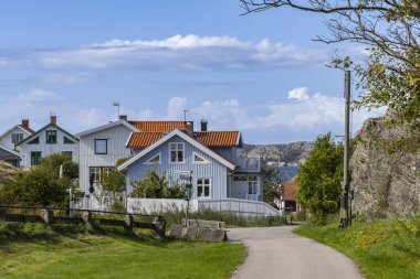 İsveç 'in Tjorn kıyısındaki Stora Dyron adasındaki parlak İsveç sahil evleri, açık mavi gökyüzünün altında, kırmızı kiremitli çatıları ve beyaz çitleri var. Huzurlu, aile dostu deniz manzarası.
