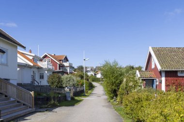 İsveç 'in Tjorn kıyısındaki Stora Dyron adasındaki parlak İsveç sahil evleri, açık mavi gökyüzünün altında, kırmızı kiremitli çatıları ve beyaz çitleri var. Huzurlu, aile dostu deniz manzarası.