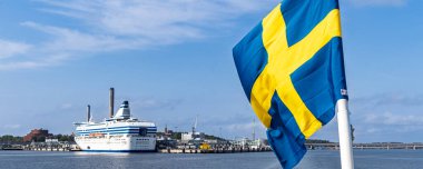 İsveç 'in Stockholm limanında İsveç bayrağıyla demirlemiş bir yolcu gemisi. Şehir manzarası, seyahat ve İsveç yaşam tarzı temaları için ideal.