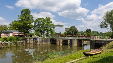 Belçika 'nın Doğu Flanders kentindeki Astene yakınlarındaki Leie nehrinin üzerinde renkli çiçek sepetleri olan eski yeşil asma köprü. Eski bir kayık kırsal manzarayı tamamlıyor..