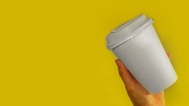 Kahve için kağıt bardak sarı zemin üzerinde elleri ısıtır, metin afişi için alanı kopyalar