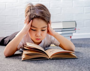 Yorgun küçük çocuk evde kitap okuyarak yerde yatıyor. Evde eğitim. Evde kal.