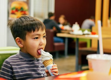 Küçük mutlu çocuk öğle yemeği sırasında bir kafe restoranında külahta beyaz dondurma yiyor. çocukluk ve mutluluk kavramı.