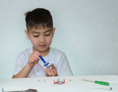 Beş yaşında bir çocuk beyaz bir masada oturuyor ve elektronik yapıcıyı oynuyor, bir metal yapıcıyı tornavida, cıvata ve fındıkla birleştiriyor. Ev hayatı, kendini yetiştirme..