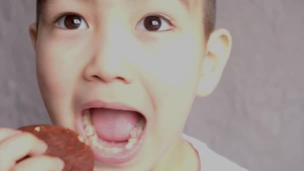 Хлопчик без зубів кусає шоколадний чіп. Крупним планом. дитина їсть Choco Пиріг, смачний, солодкий, солодкий зуб на сірому фоні — стокове відео