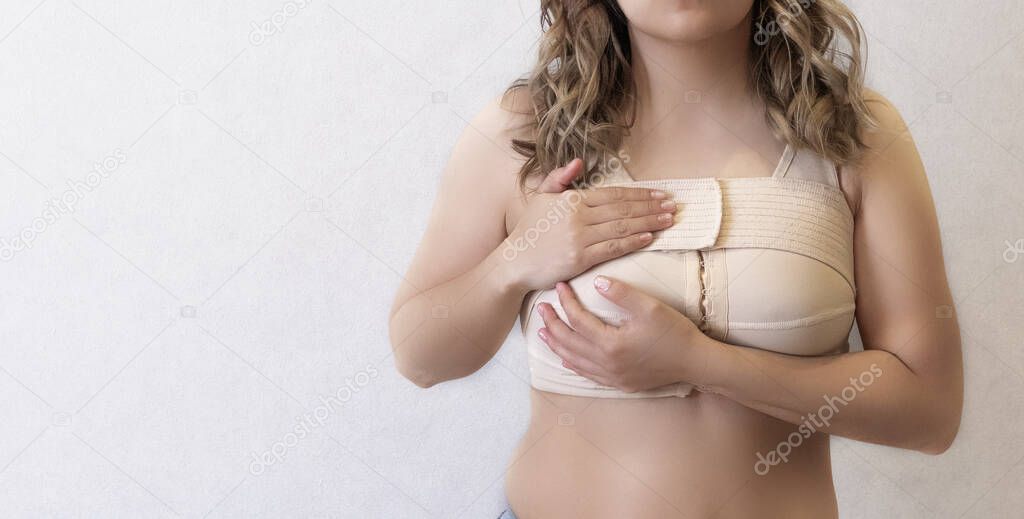 Young woman in beige compression bra bandage after breast augmentation surgery mammoplasty. banner. advertising. copy space.